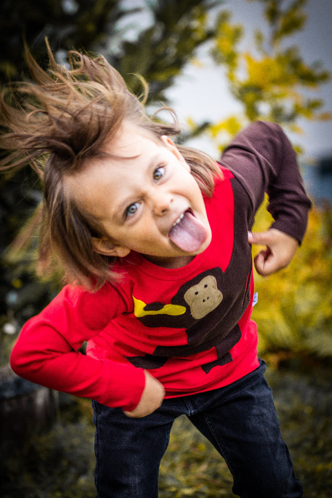 Ein ausgelassen spielendes Kind mit einem roten Pullover mit einem Affen Tiermotiv von Luanimals